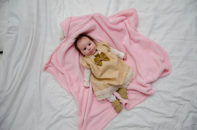 Bábätko v zlatých šatách leží na ružovej deke na posteli.jpg