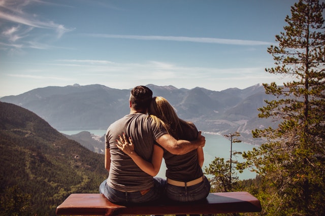 Muž a žena sedia v objatí a pozerajú na hory a jazero.jpg
